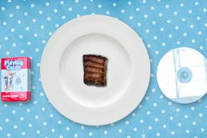 A 100-calorie serving of steak on a plate next to a pack of cards and a CD