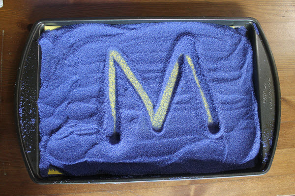 letter M and a colored background in a salt tray