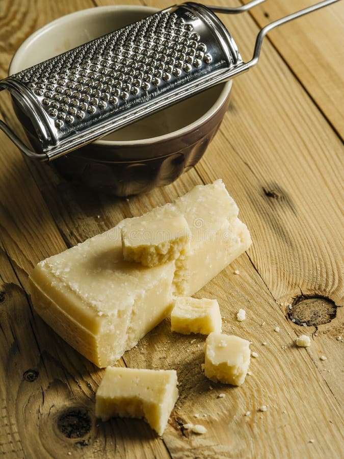 Block of parmesan cheese and grater. Block of parmesan cheese on a wooden table with grater in the background stock images