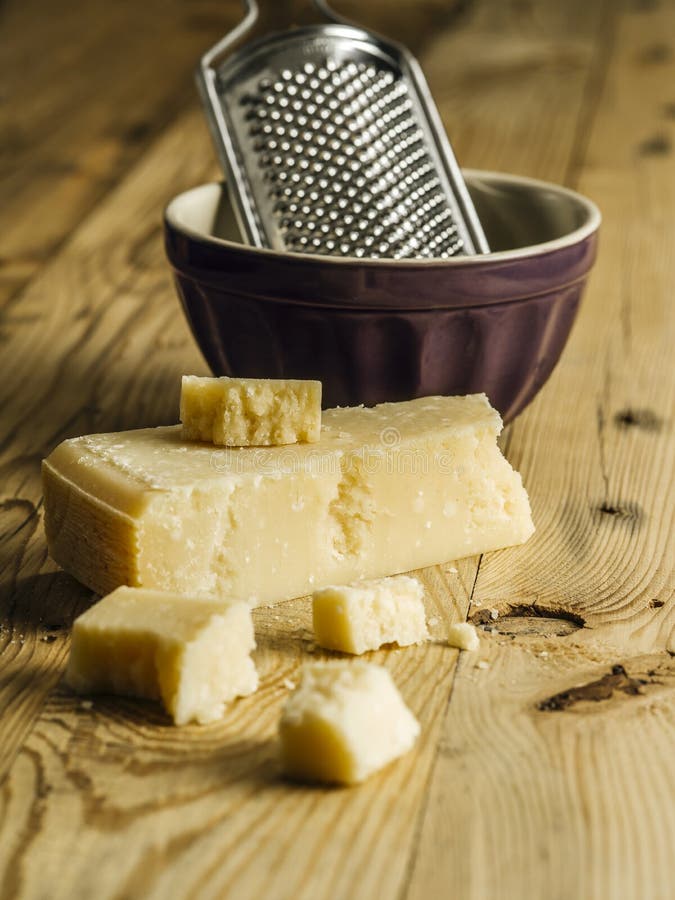 Block of parmesan cheese and grater. Photo of a block of parmesan cheese on a wooden table with grater in the background stock photography