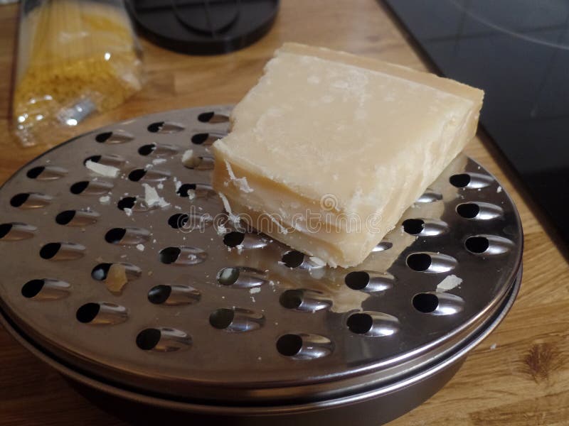 Block of Parmesan cheese on top of a grater. Block of Parmesan cheese on top of a cheese grater with spaghetti in the background stock image