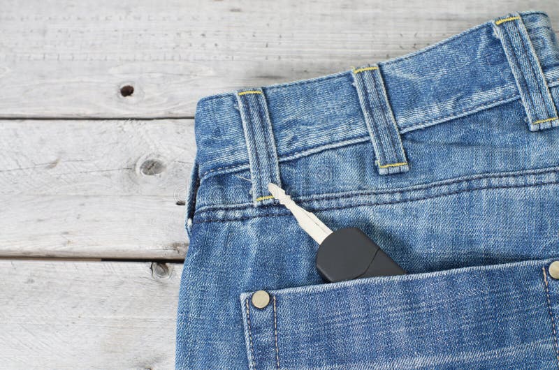 Car key in blue jeans back pocket. Against wooden background stock image