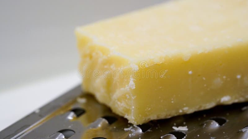 Cheese on a cheese grater. Close up of a block mozzarella cheese on a metal cheese grater, bright background stock photography