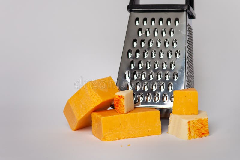 Cheese grater and blocks of cheddar cheese on solid background. On solid ba