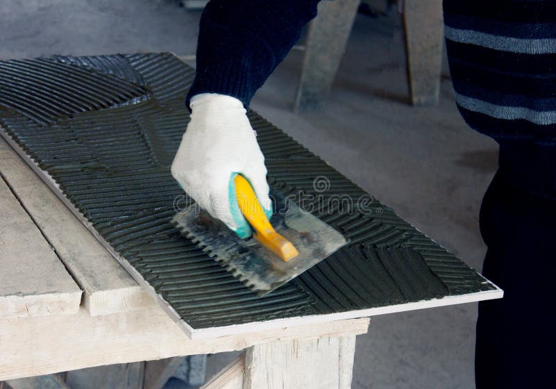 Close up of a builder, a tiler sitting in a glue spreading on a tile stock image