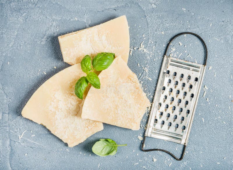 Cuts of Parmesan cheese with metal grater and fresh basil over concrete textured background. Top view stock image