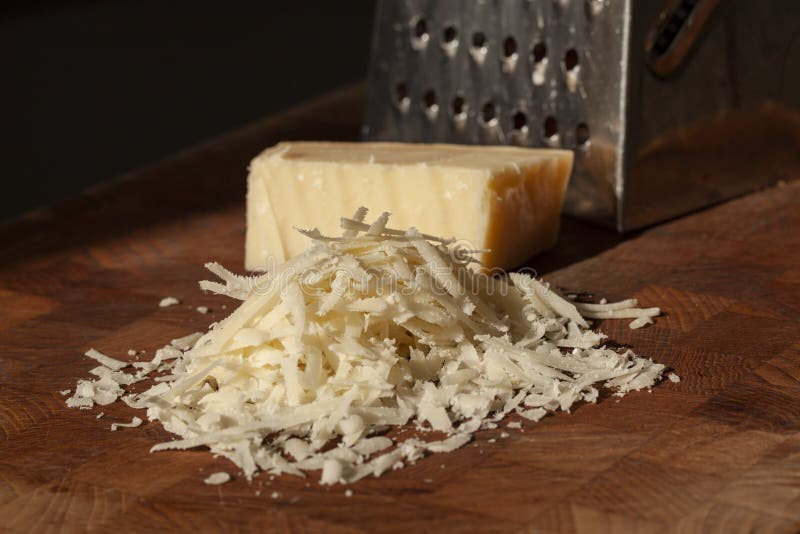 Grated italian parmesan cheese on wooden chopping board with a block of parmasan and a grater in the background. Close up photo. With selective focus stock images