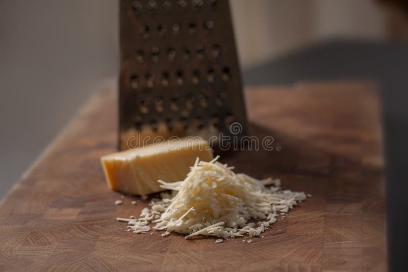 Grated italian parmesan cheese on wooden chopping board with a block of parmasan and a grater in the background. Close up photo. With selective focus stock image