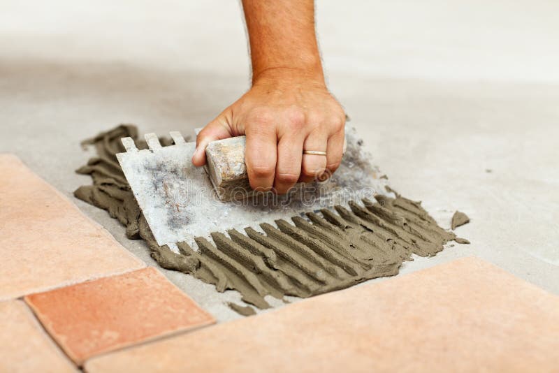 Laying ceramic floor tiles. Man hand spreading adhesive material, closeup stock photo