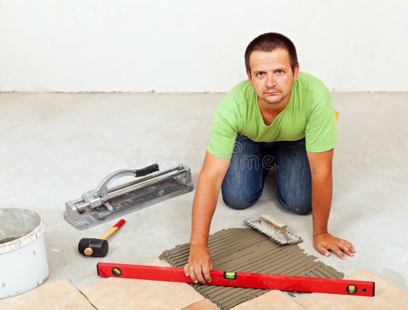 Man laying ceramic floor tiles on concrete floor. Checking his work with a spirit level royalty free stock photography