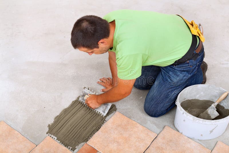 Man laying ceramic tiles floor - spreading the adhesive. Man laying ceramic tiles floor, spreading the adhesive on the concrete - focus on hands stock photo