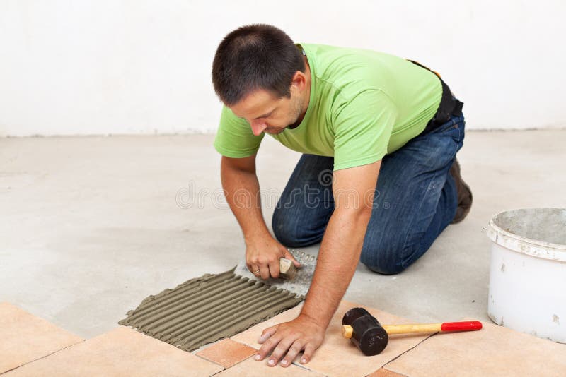 Man laying floor tiles - spreading the adhesive. Man laying ceramic floor tiles - spreading the adhesive material stock photo