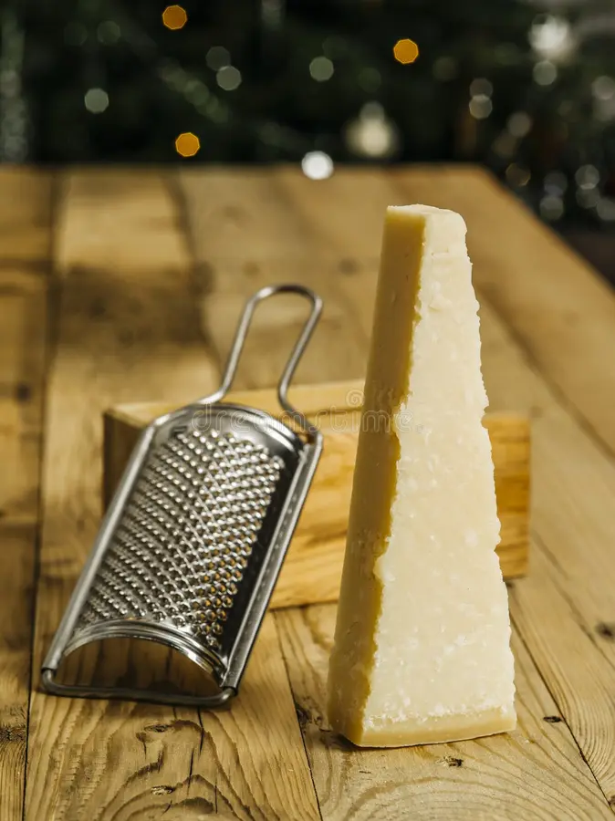 Block of parmesan cheese and grater. Photo of a block of parmesan cheese on a wooden table with grater in the background royalty free stock image