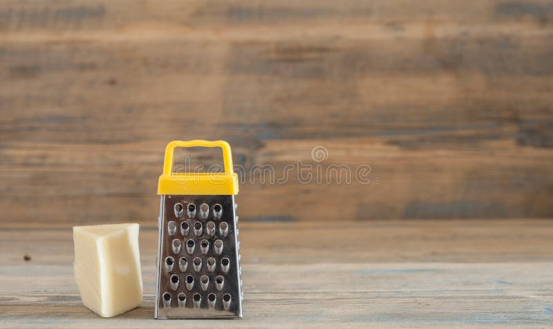 Steel grater and cheese on wooden board. Cheese and steel grater on a wood kitchen table royalty free stock photos