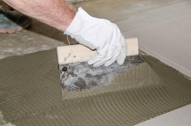 Tiler spreading tile adhesive on the floor. Laying tiles, tiler spreading tile adhesive on the floor stock image