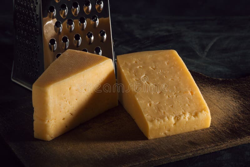 Two pieces of cheese and grater on a board against a dark background.  stock images