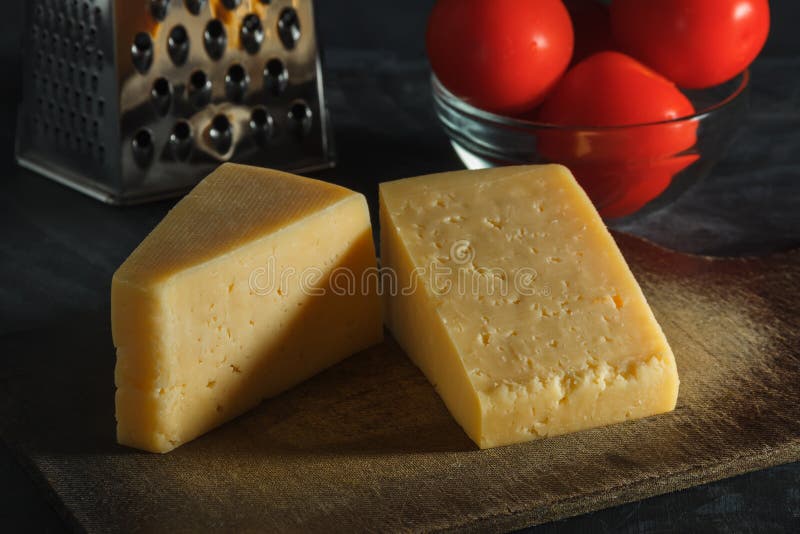 Two pieces of cheese, tomatoes and grater on a board on a dark background.  stock photo